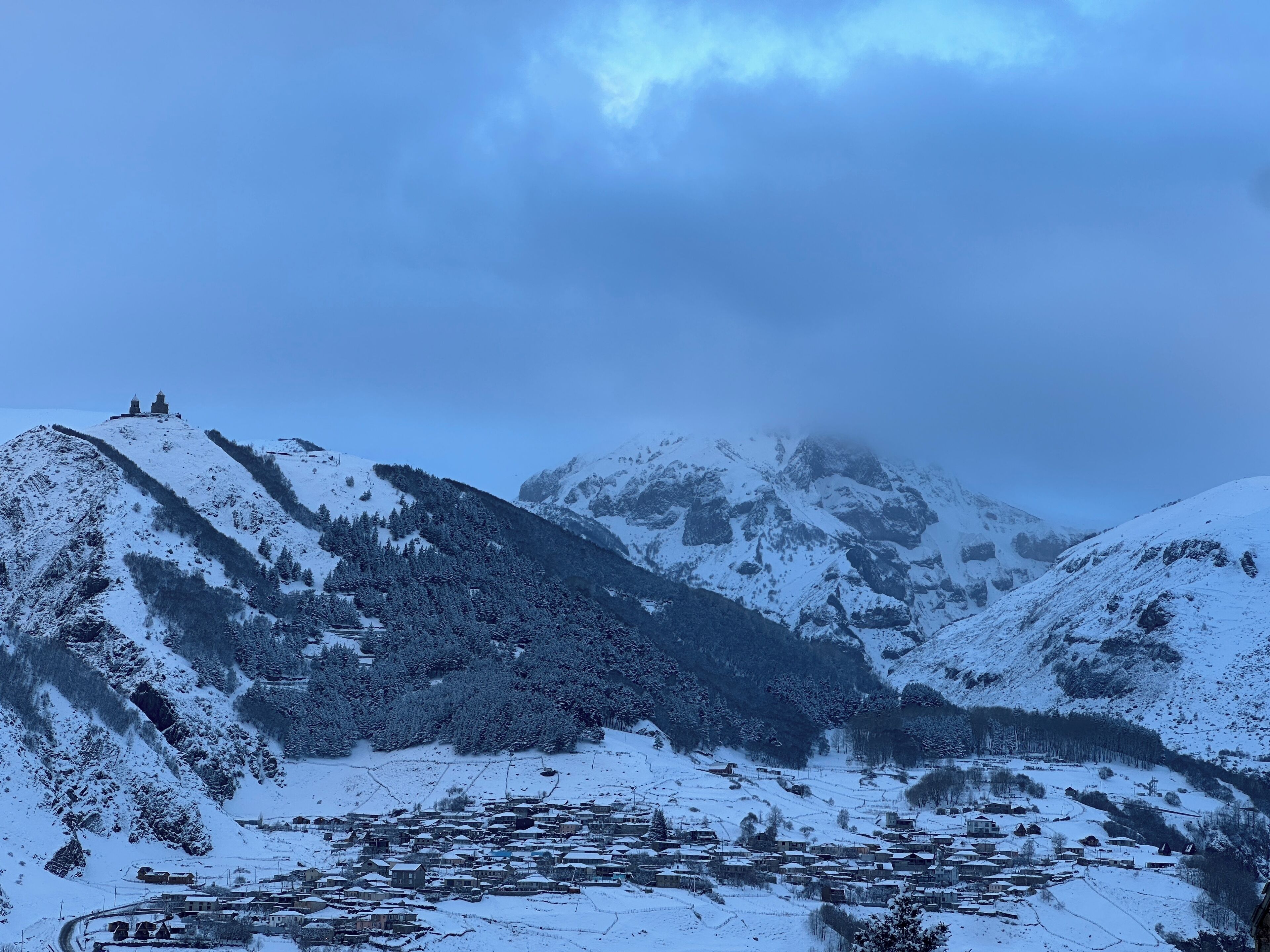Un pueblo cubierto de nieve en la montaña con edificios e iglesia en una colina.