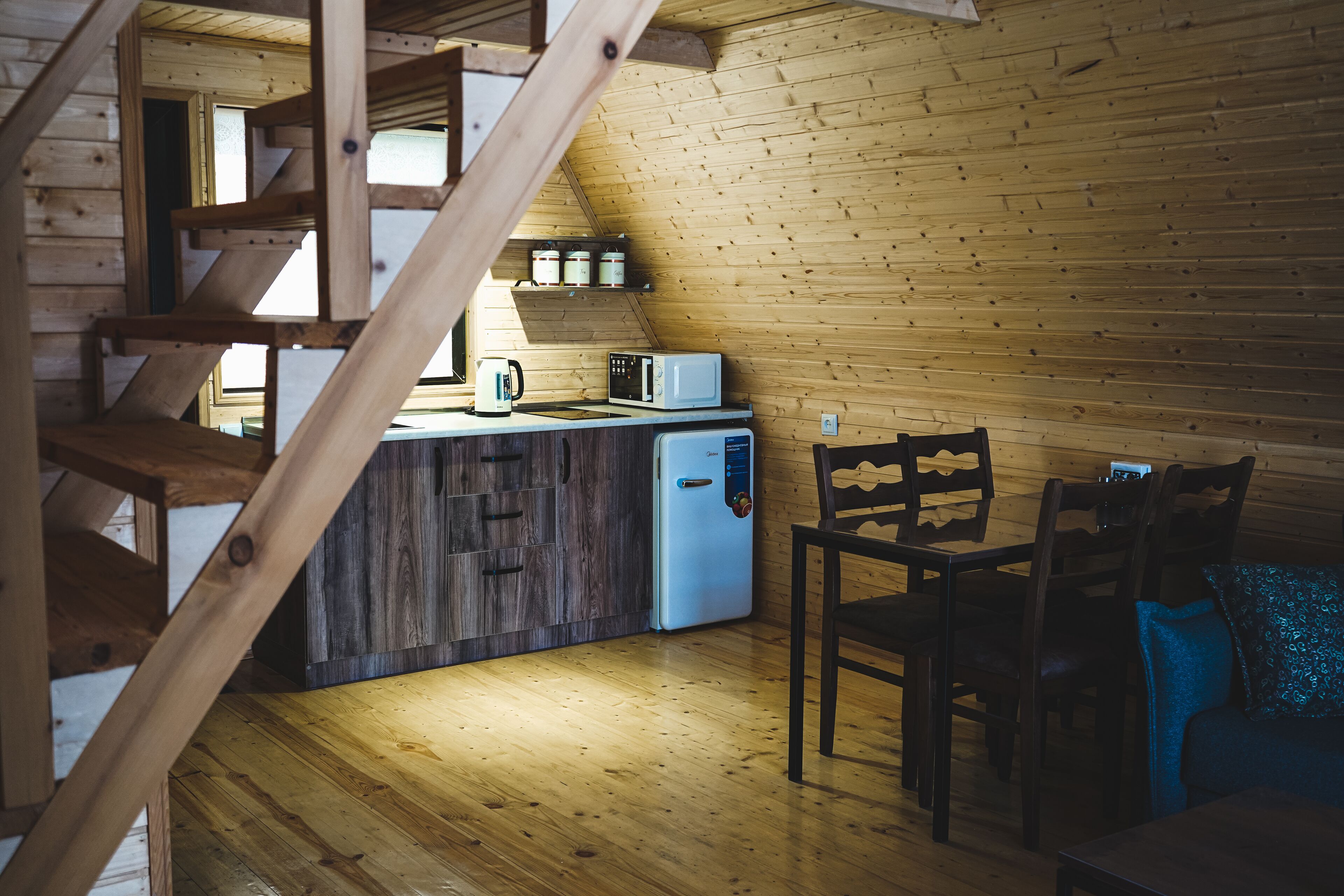 Un interior de madera con zona de cocina, que incluye un microondas, un refrigerador y una escalera de madera.