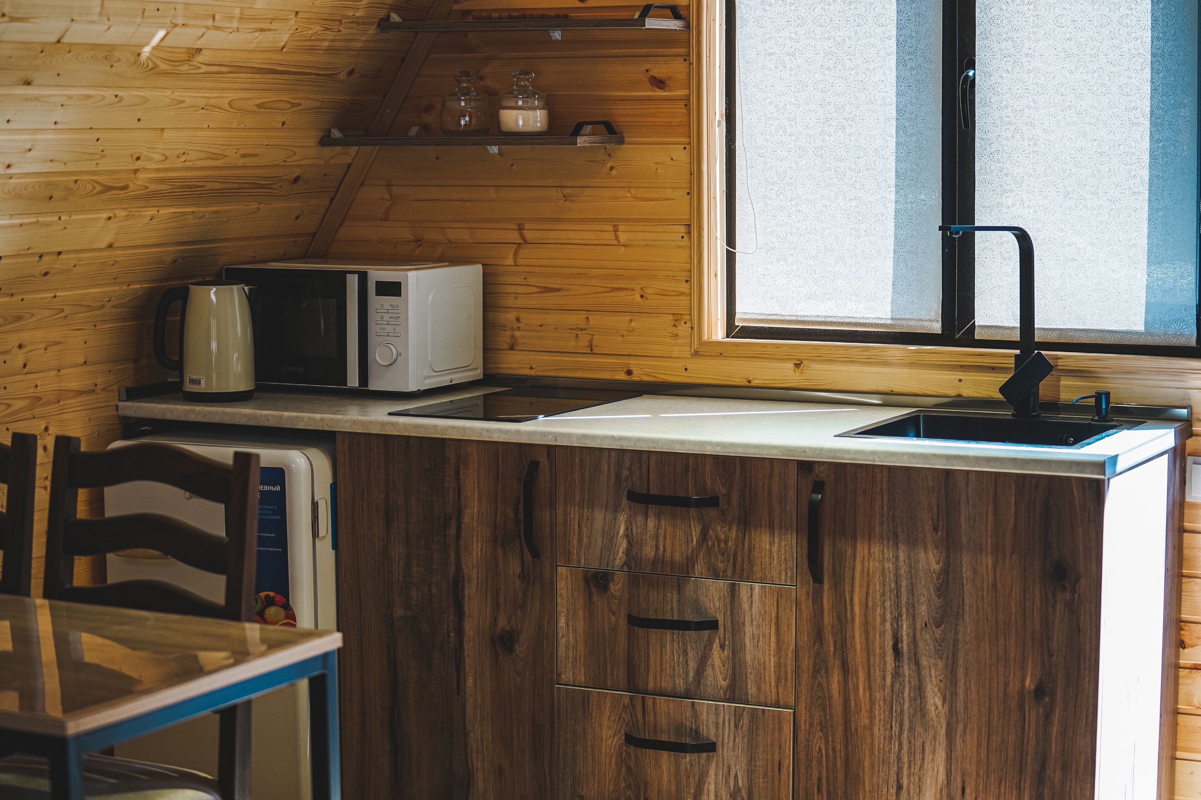 A compact kitchen with wooden cabinetry, a microwave, a kettle, and a window with a view.