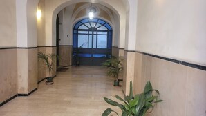 Un couloir aux plafonds voûtés, agrémenté de plantes en pot et orné d’une grande fenêtre au fond.