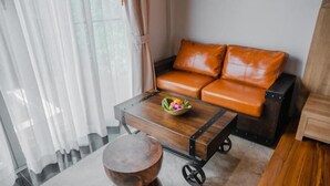 A room with a leather sofa, a wooden coffee table with a bowl, and a small round table.