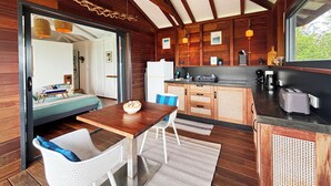 Een gezellig cabin interieur met een houten eethoek, een keuken met een zwart aanrechtblad, en een groot raam met uitzicht op groen.