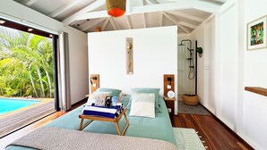 Een slaapkamer met een bed, nachtkastjes, een bedlampje, een houten vloer, een groot raam en uitzicht op een zwembad.