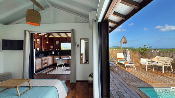 Een moderne slaapkamer met houten vloer, een bed en uitzicht op een keuken en een terras.