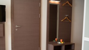 A bedroom with a bed, a wardrobe, a mirror, a hanging clothes rack, and a small table with decorative items. - Hotel Orangerie (Vienna)