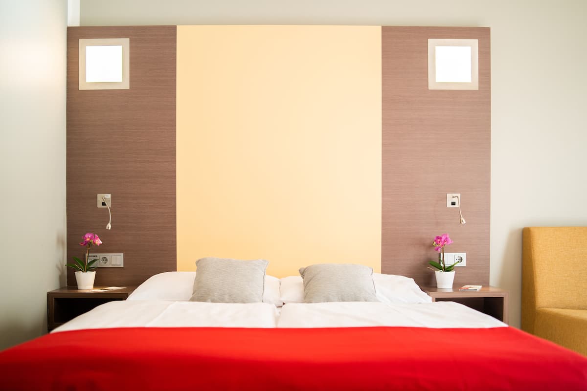 A hotel room with a bed, two nightstands, a chair, and two potted plants.