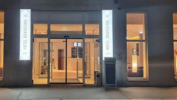 A hotel entrance with glass doors and windows, signage indicating the hotel name, and a visible reception area. - Hotel Orangerie (Vienna)