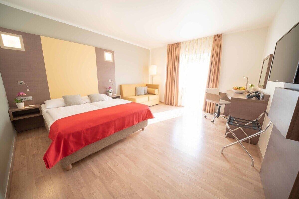 A hotel room with a bed, a desk, a chair, a TV, and a window with curtains.