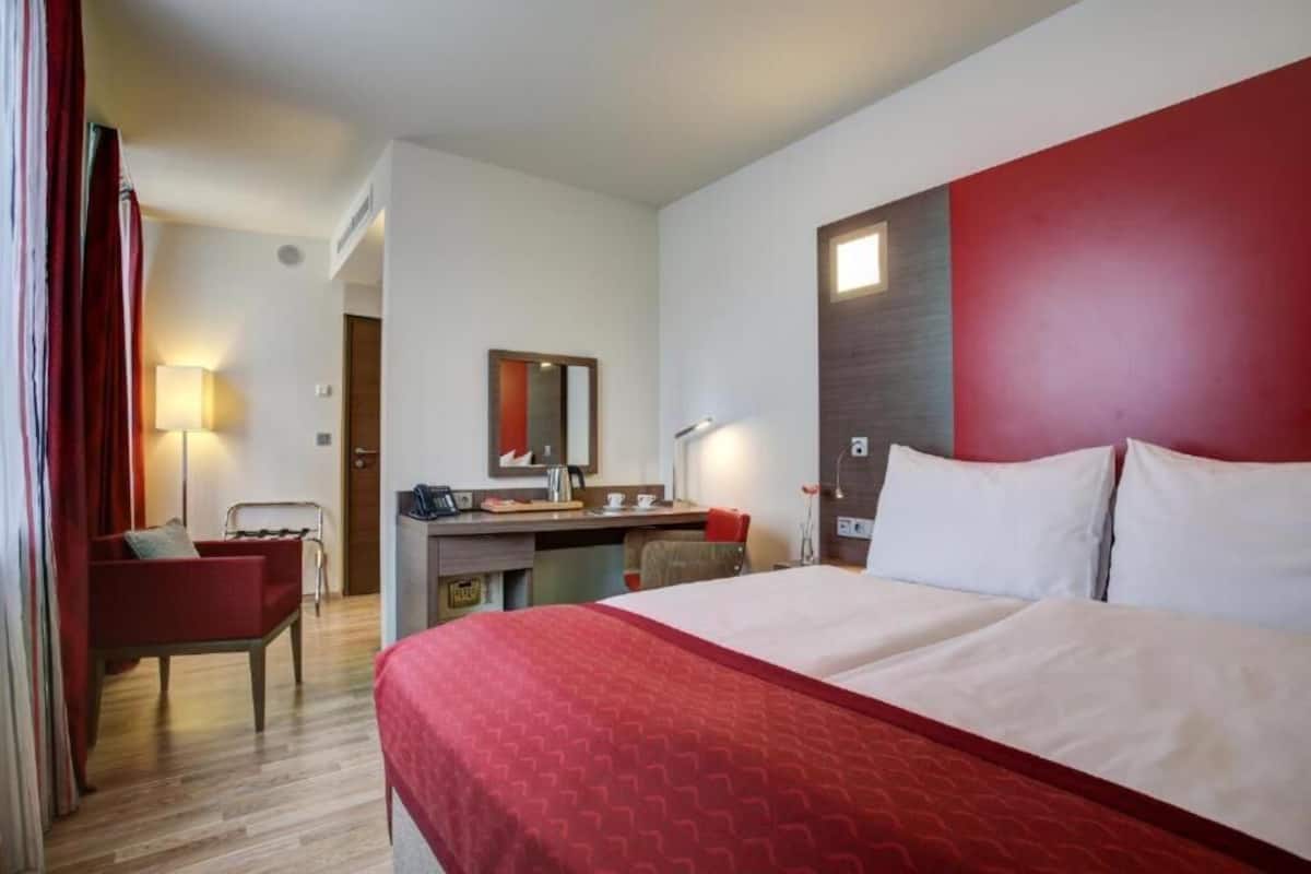 A hotel room with a large bed, a desk, a chair, and a mirror.