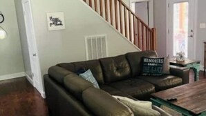 Una sala de estar con un sofá de cuero oscuro, una mesa de centro de madera y una escalera con barandilla de madera.