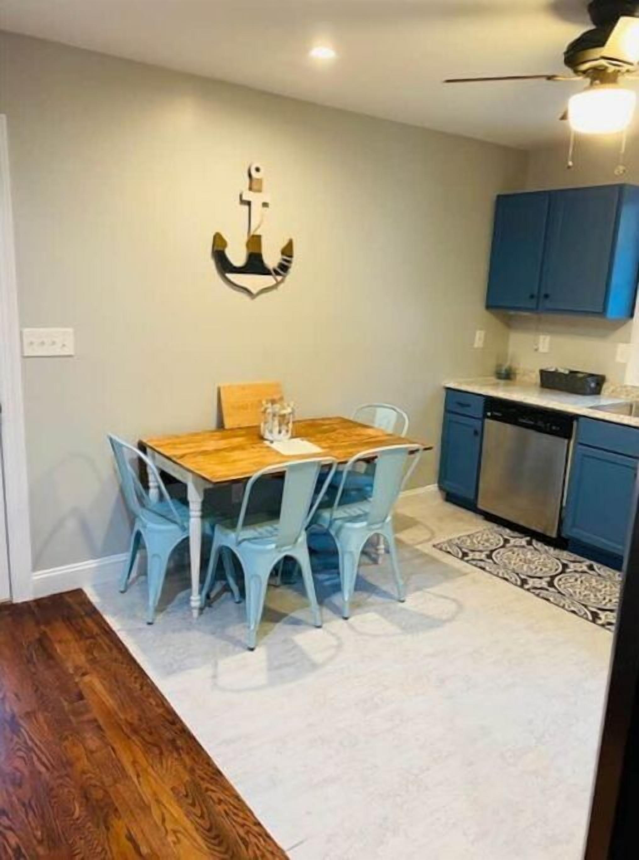 Un comedor con una mesa de madera y sillas azules, una cocina con armarios azules y un ventilador de techo.