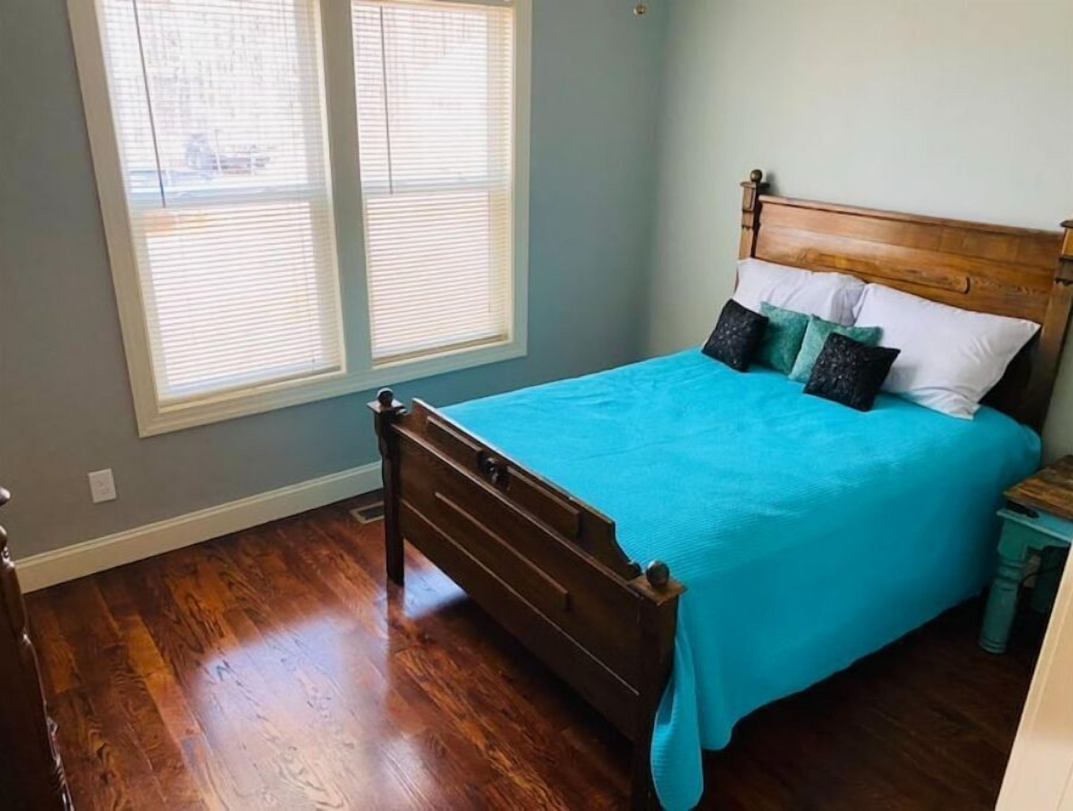 Een slaapkamer met een houten bed, een blauw beddegoed en een raam met jaloezieën.