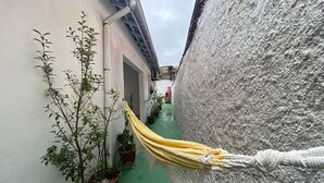 Un vialetto stretto con un'amaca gialla tesa tra due edifici, piante in vaso a sinistra e un muro strutturato a destra.
