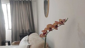 Una camera d'albergo con un letto, un tavolino con una bottiglia d'acqua, un'orchidea in vaso e uno specchio a parete.