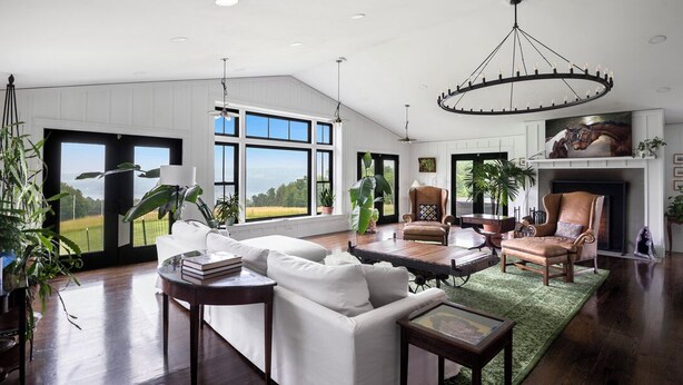 A spacious living room with a large window, a fireplace, and a chandelier. - Paradise Found. The Ultimate Skaneateles Lake Retreat. (Skaneateles)