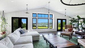 A spacious living room with a large window offering a view of the outdoors, a white sofa, a wooden coffee table, and a comfortable armchair. - Paradise Found. The Ultimate Skaneateles Lake Retreat. (Skaneateles)