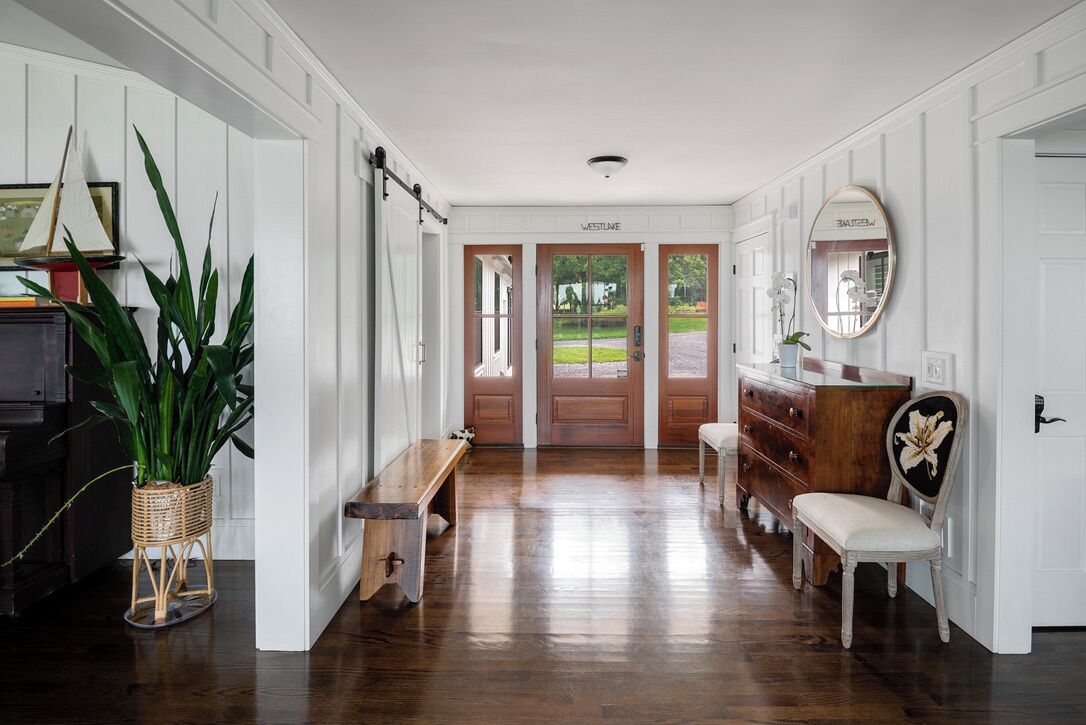Een gang met houten vloer, een bankje, een dressoir en een spiegel.