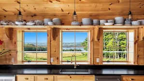 A wooden cabin kitchen with a large window, a sink, and cabinets. - Paradise Found. The Ultimate Skaneateles Lake Retreat. (Skaneateles)