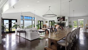 A spacious dining area with a long wooden table and multiple chairs, surrounded by large windows offering views of the outdoors. - Paradise Found. The Ultimate Skaneateles Lake Retreat. (Skaneateles)