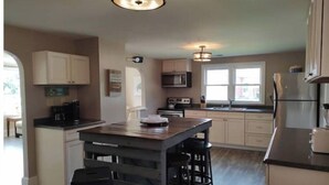 A modern kitchen with a central island, bar stools, and a large window providing natural light. - Bowline Knot - On the ICW - Dog Friendly! (Coinjock)