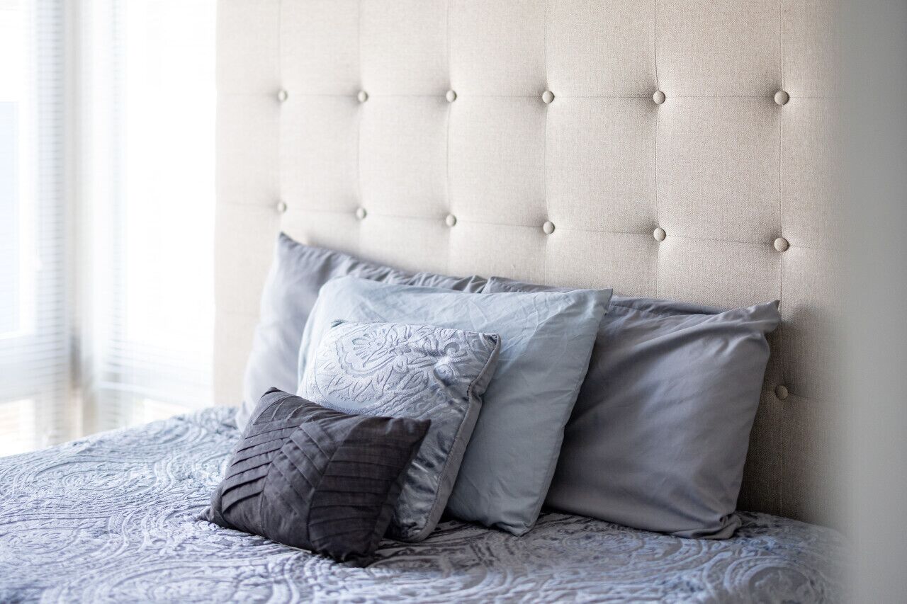 Una cama con cabecera capitonada y muchas almohadas.