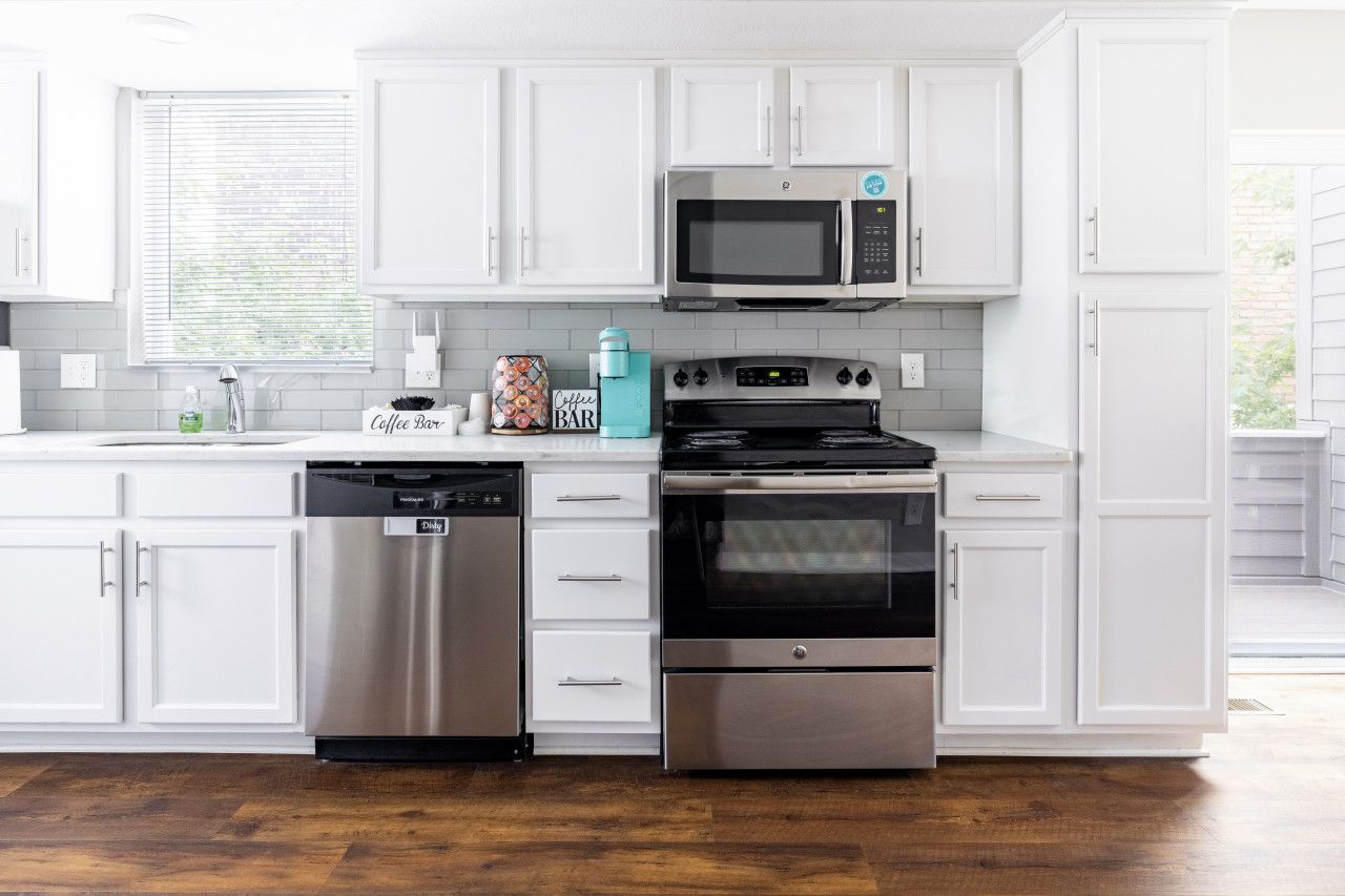 A modern kitchen with white cabinets, a stainless steel dishwasher, a microwave, and a stove.