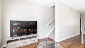 Een moderne woonkamer met een flatscreen televisie op een houten standaard, een glazen salontafel, en een trap die naar een hoger niveau leidt.
