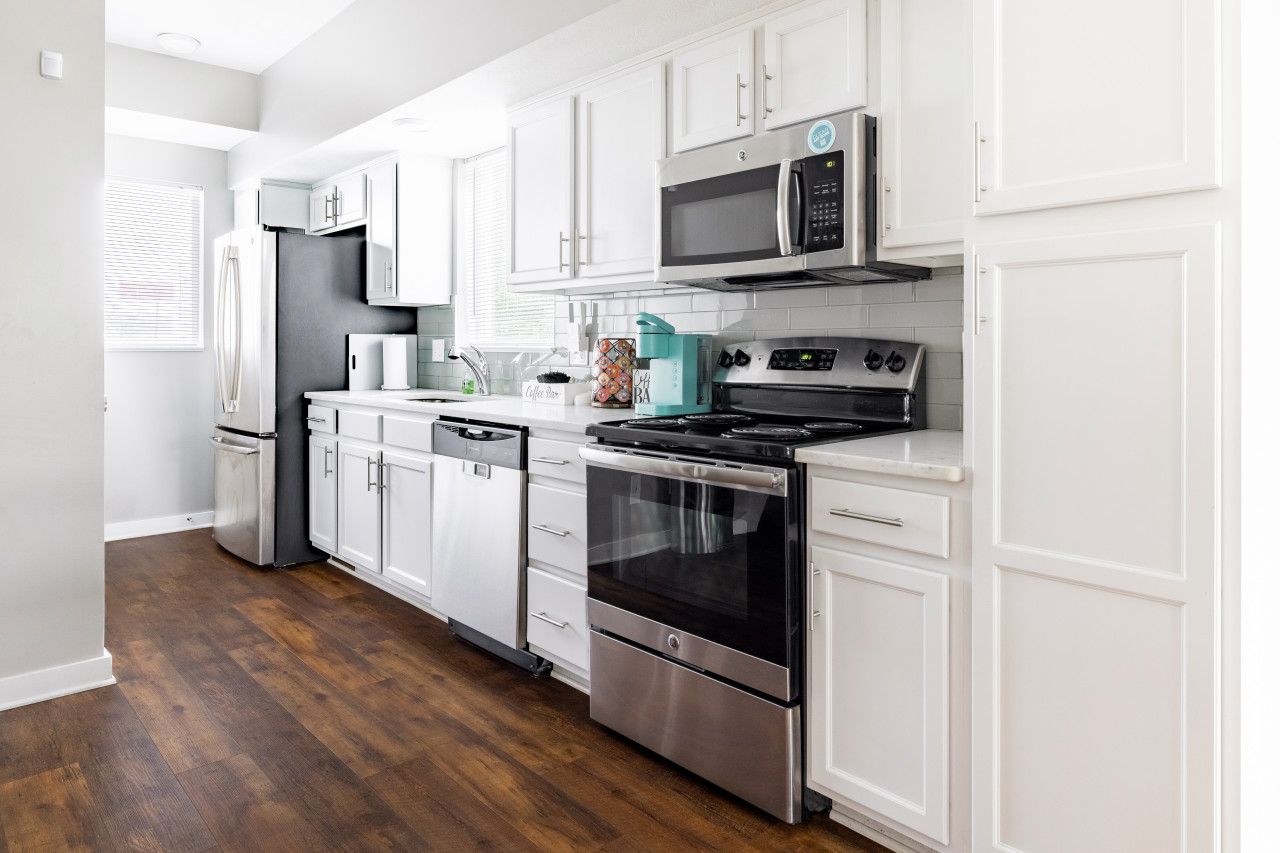 Une cuisine moderne avec des meubles blancs, des appareils en acier inoxydable et un plancher en bois foncé.
