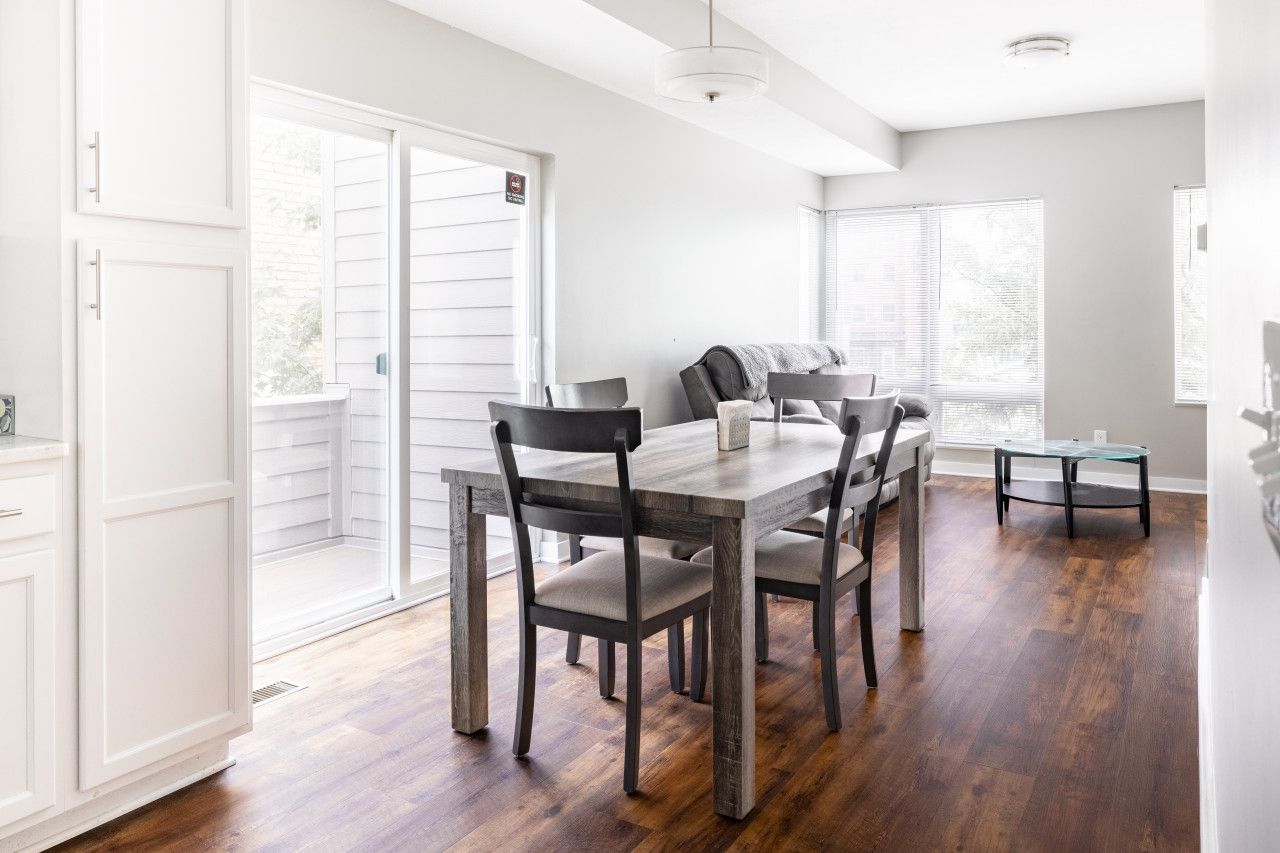 Zona de menjador amb taula i cadires de fusta, una banca i vistes a l'exterior a través de grans finestres.