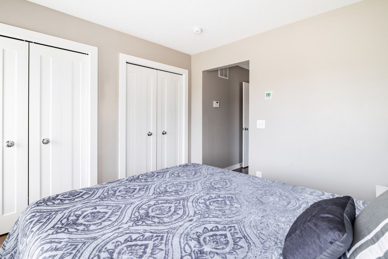 A bedroom with a patterned bedspread, a gray pillow, and white wardrobes.