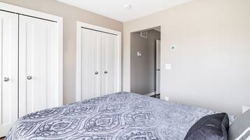 A bedroom with a patterned bedspread, a gray pillow, and white wardrobes.