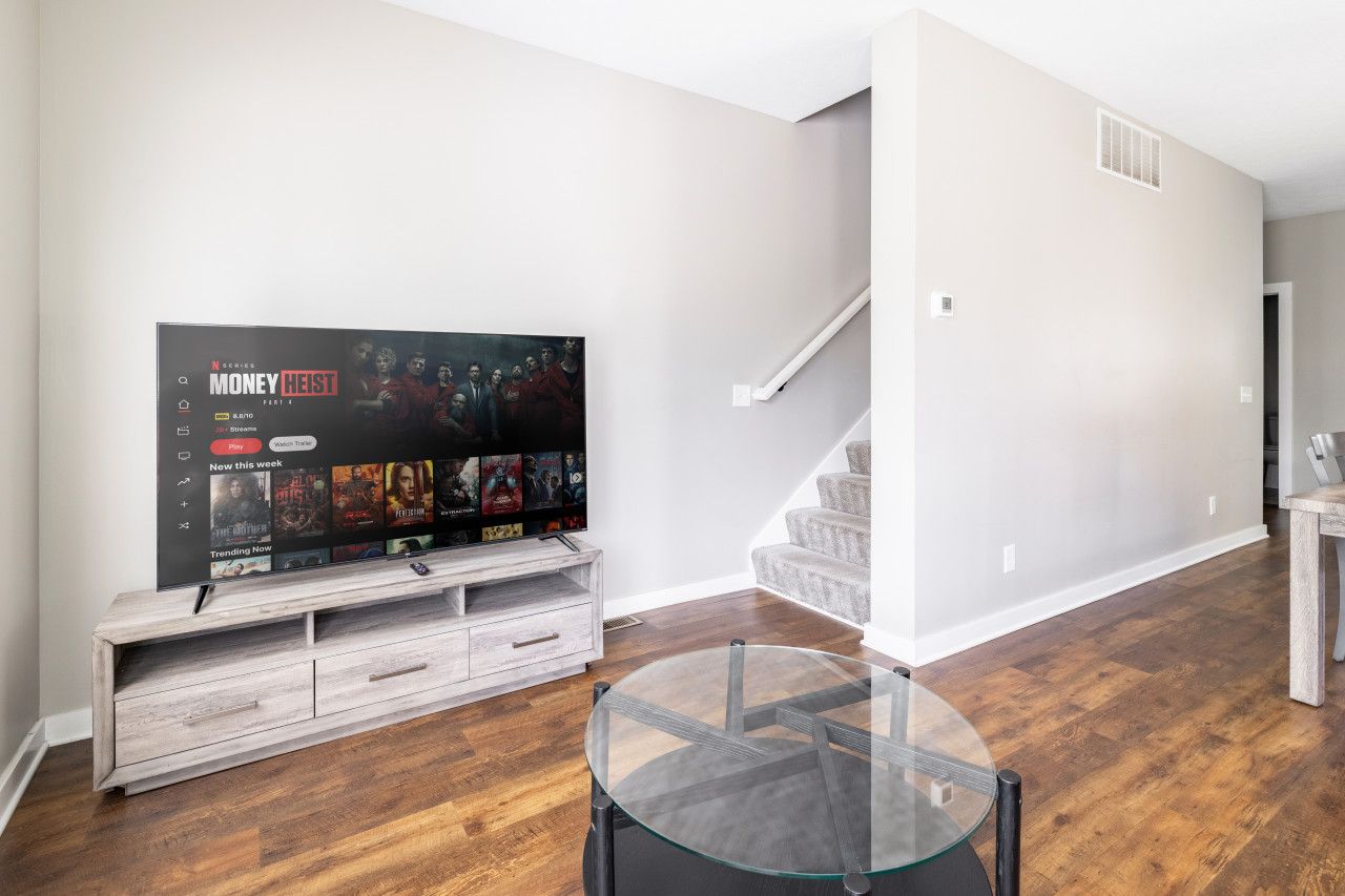 A modern living room with a flat-screen TV on a wooden stand, a glass coffee table, and a staircase leading to another level.