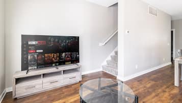 A modern living room with a flat-screen TV on a wooden stand, a glass coffee table, and a staircase leading to another level.
