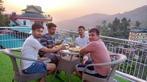 Un grupo de personas cenando en una mesa en un balcón con vistas a un paisaje montañoso.
