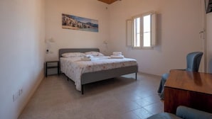 Une chambre à coucher avec un lit, un bureau, une chaise, une fenêtre et un tableau accroché au mur.