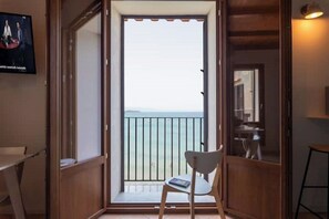 Una habitación con vista al mar, una silla, una mesa y un televisor en la pared.