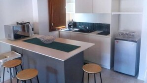 Une cuisine compacte dotée d’un îlot central, d’un évier, d’un four à micro-ondes et d’un réfrigérateur. Deux tabourets sont placés autour de l’îlot.