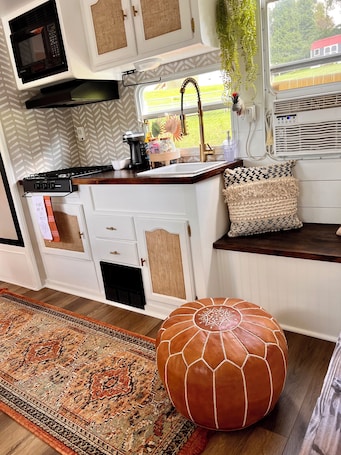 A compact kitchenette with a microwave, stove, sink, and window with a view of greenery.