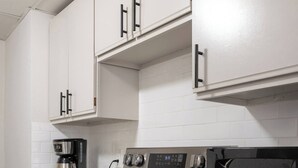 Eine moderne Küche mit weißen Schränken, Edelstahlgeräten, darunter ein Backofen, eine Mikrowelle und eine Kaffeemaschine, sowie einem Geschirrspüler.