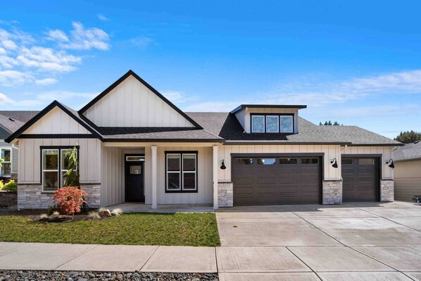 Stylish two-story home with a gable roof and garage, set amidst a beautifully landscaped yard.