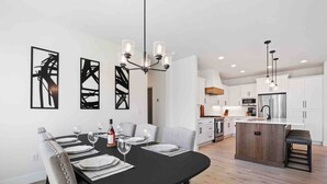A modern kitchen with white cabinets, a central island, and a dining area with a black table and grey chairs. - Prestine and Comfortable Home (Brush Prairie)