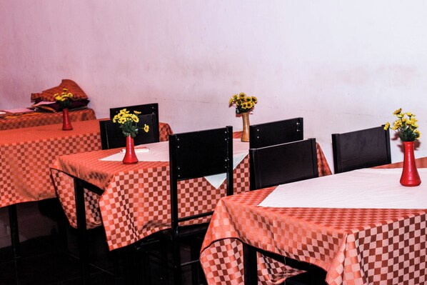 A restaurant with checkered tablecloths, red vases with yellow flowers, and black chairs. - Mbale Travellers Inn (Mbale)