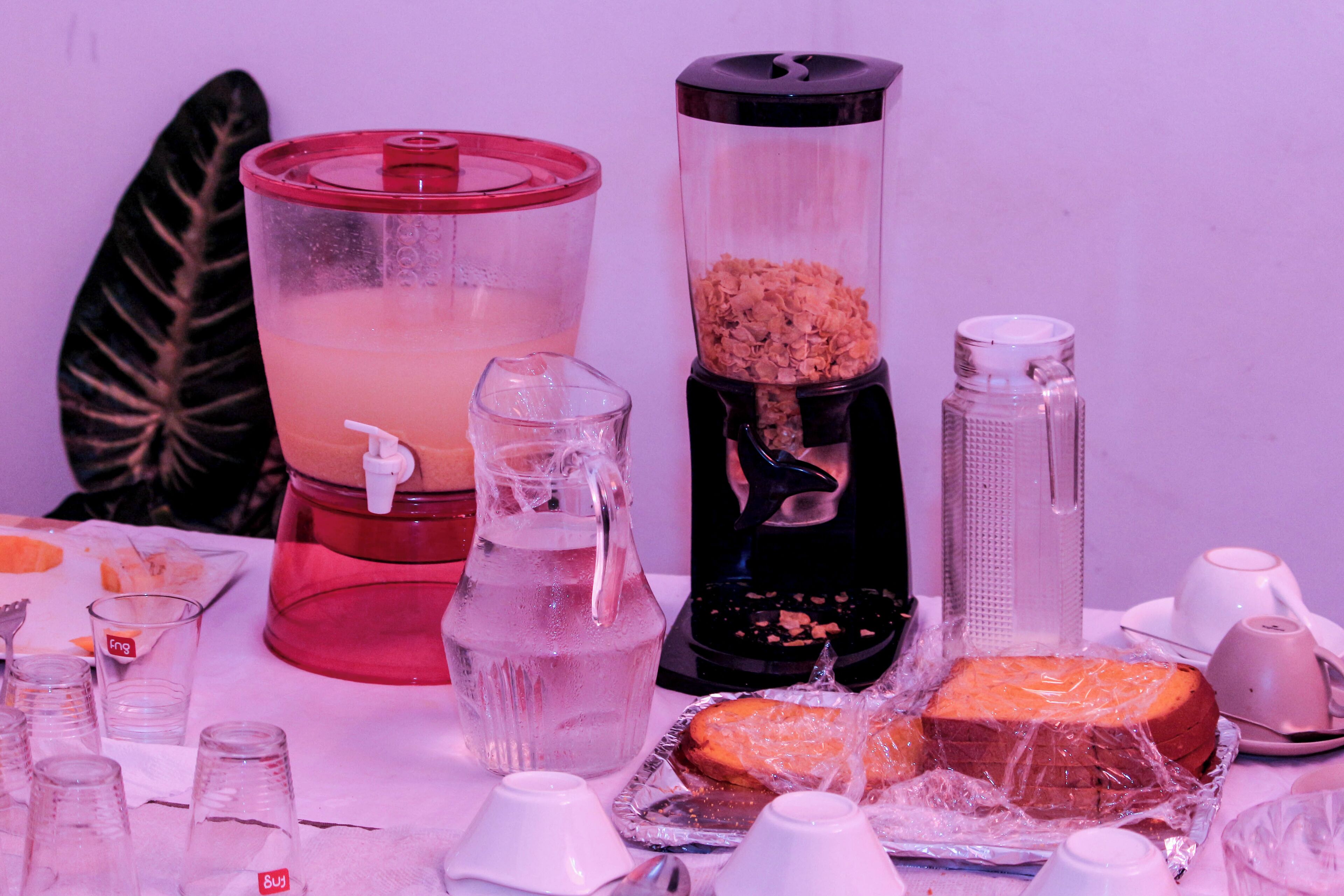 A table with various items including a pitcher, a blender, a glass, and a wrapped cake.