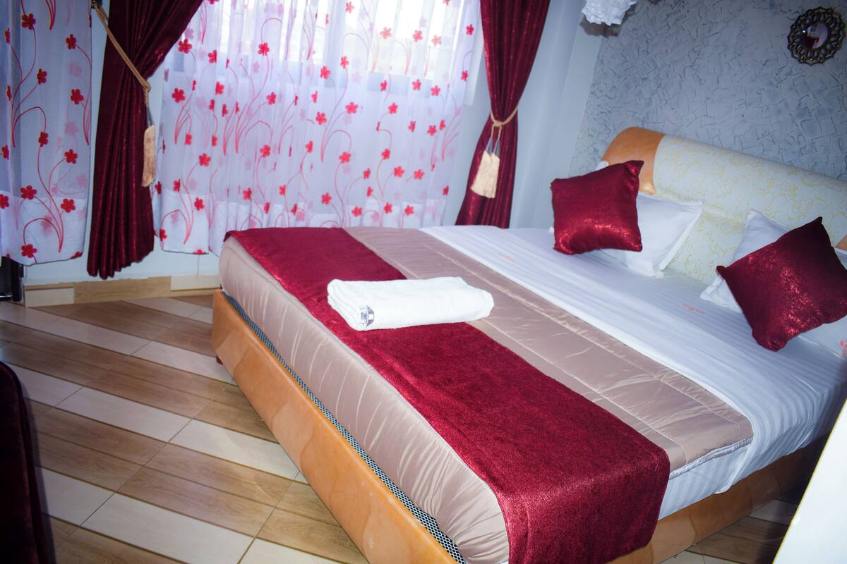 Un lit bien fait, avec une couvre-lit rouge et beige, des oreillers blancs et un plaid rouge.