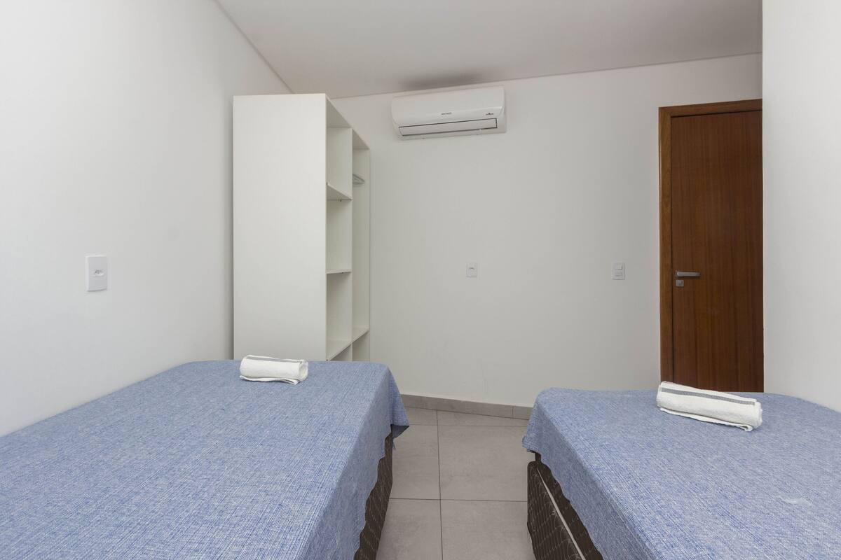 Una habitación pequeña y limpia con dos camas individuales, una puerta de madera, un equipo de aire acondicionado blanco y un armario blanco.