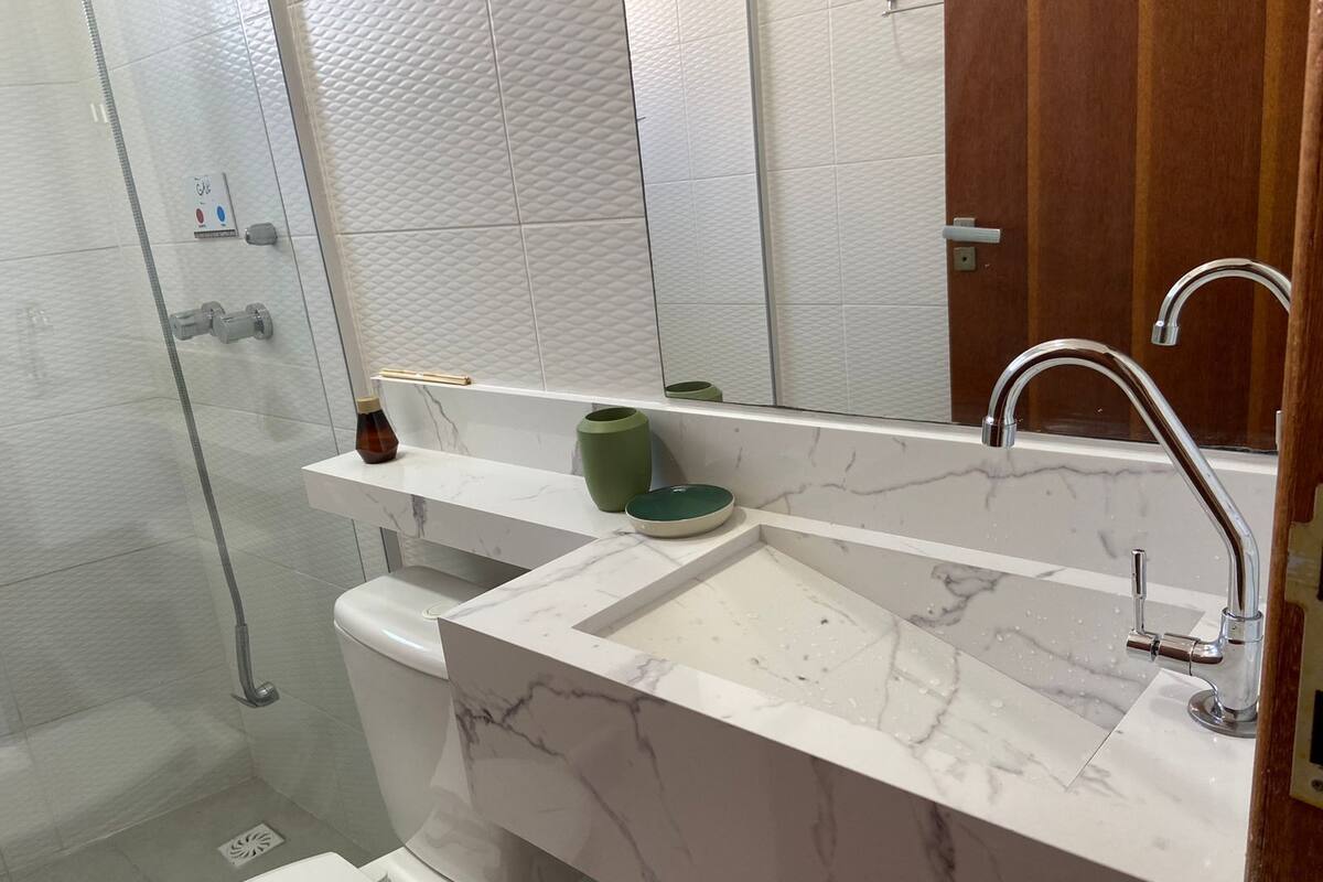 Un baño moderno con lavamanos de mármol, cabina de ducha con paredes de vidrio y puerta de madera.