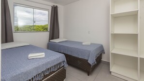 Una habitación con dos camas, una ventana con cortinas y un estante blanco.