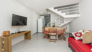 Una sala de estar moderna con un televisor de pantalla plana, un banco de madera, una mesa de comedor con sillas, un sofá rojo y una escalera.