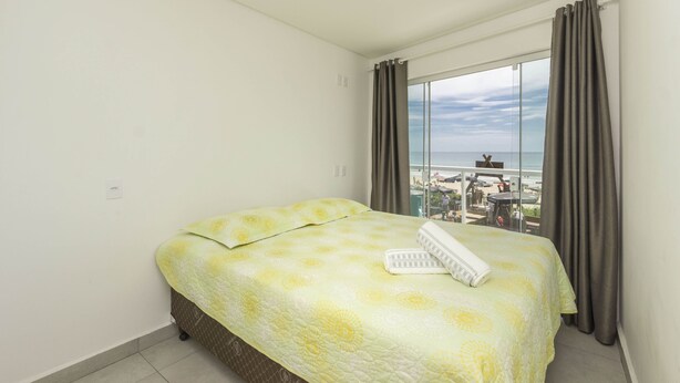 Un cuarto de hotel con una cama, una ventana con cortinas y vista a la playa.