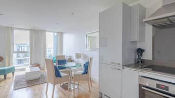 A modern apartment with a dining area, kitchen, and large windows.